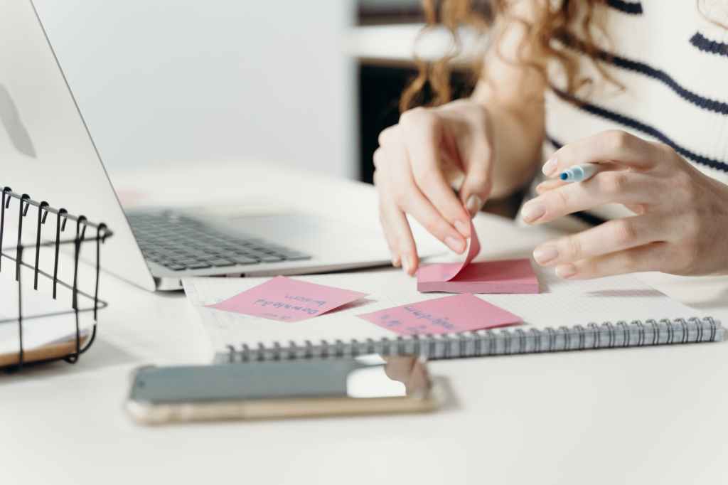 person writing on a pink sticky note